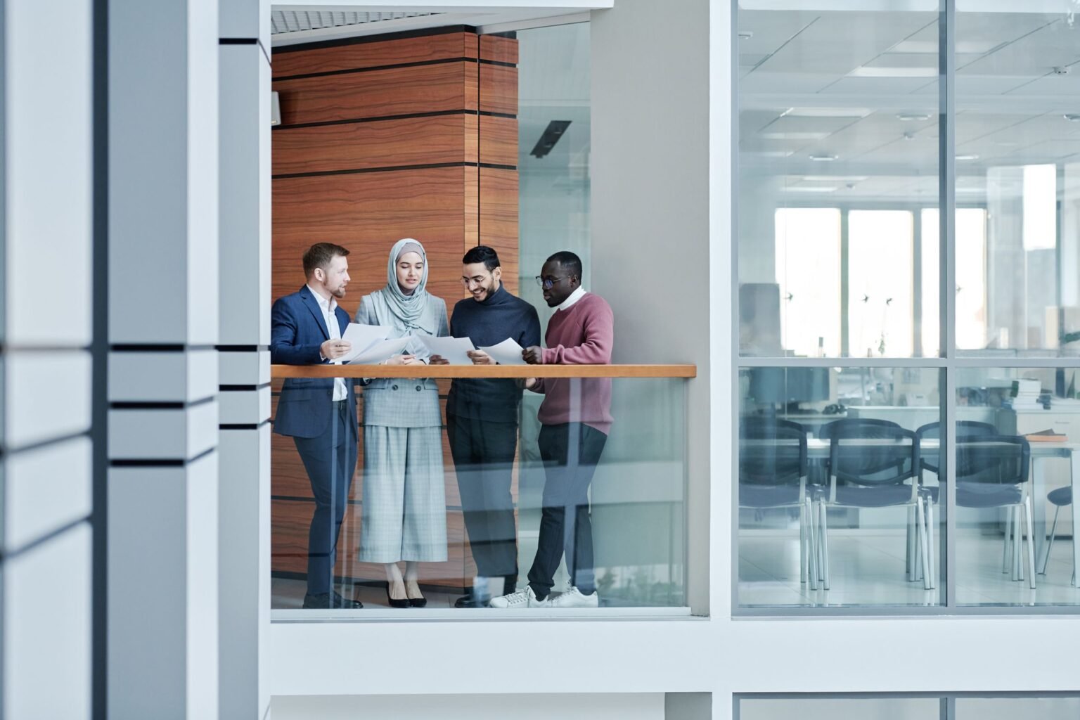 An office seen through glass, colleagues meeting in the distance.