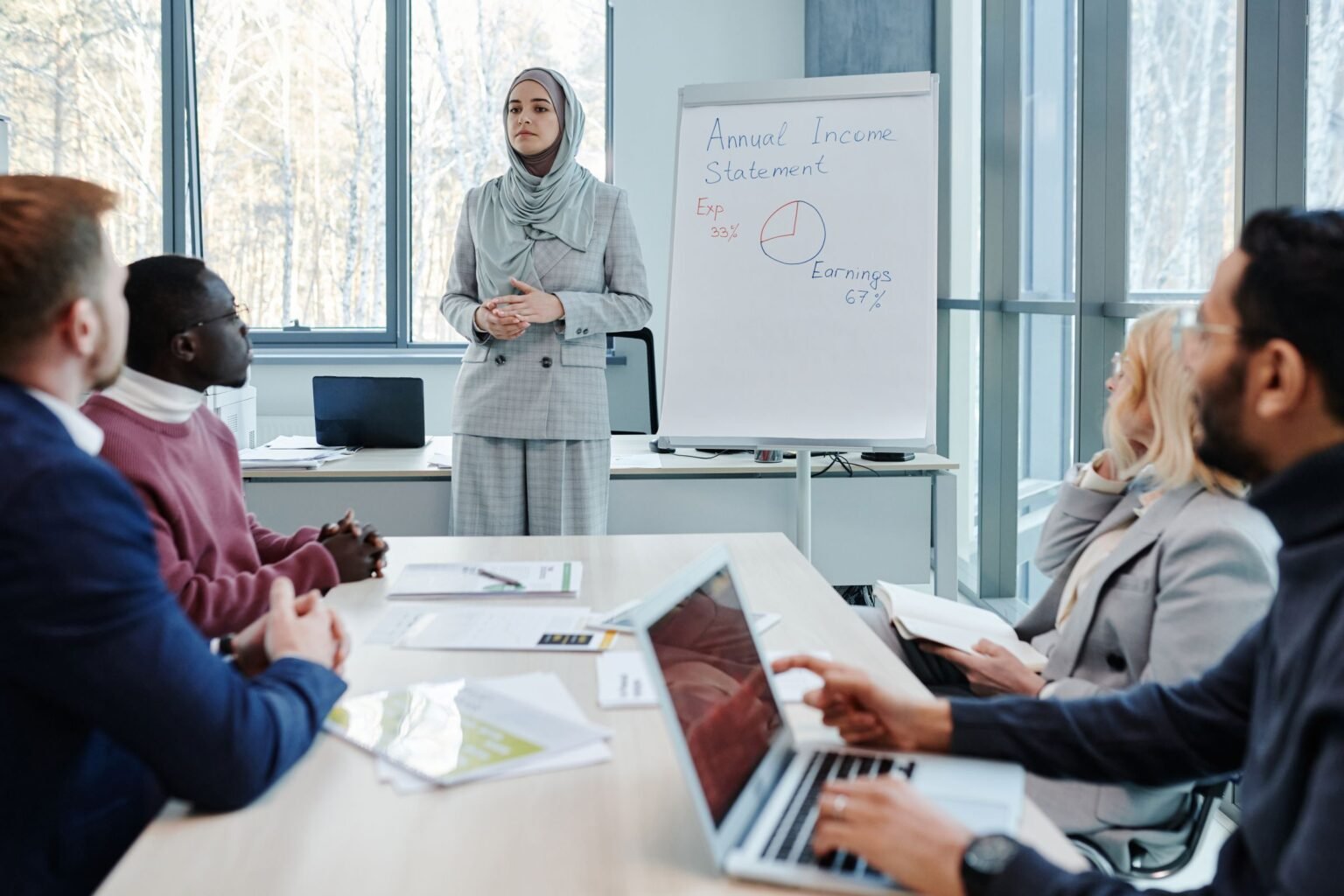 A working session in a bright meeting room, one colleague presenting to the group.