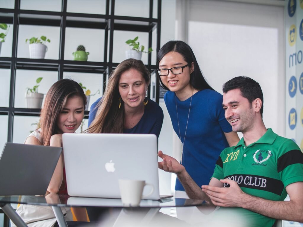 Four colleagues from different backgrounds working together around a laptop.